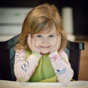 Portrait of smiling girl with hands on chin sitting at home