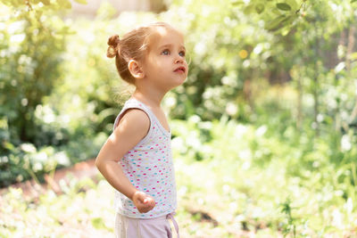 Girl looking away while standing against plants