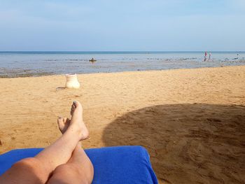 Low section of woman relaxing on beach against sky