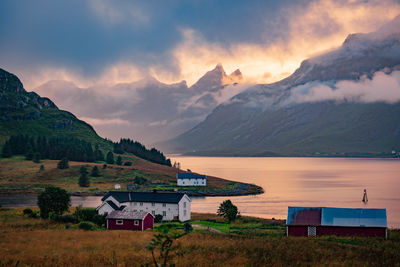 Houses by lake against mountains during sunset