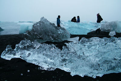 People standing on rock by sea against clear sky