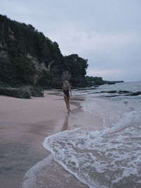 Rear view of woman standing at beach against sky