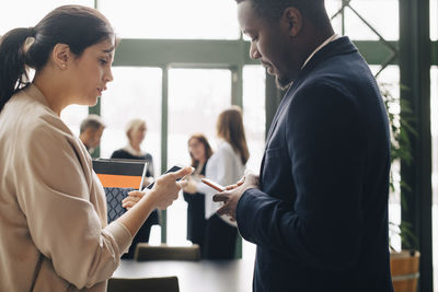 Businessman using phone while talking with female coworker in meeting at office