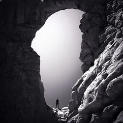 Man standing at the edge of cave against clear sky