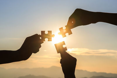 Silhouette hand holding sun against sky during sunset