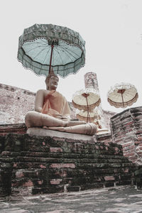 Man sitting on built structure against sky