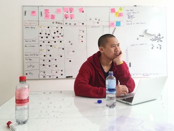 Man with hand on chin sitting by laptop in office