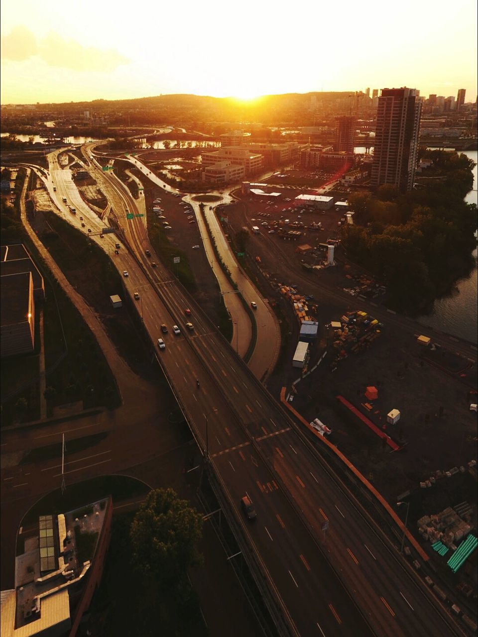 city, high angle view, city life, cityscape, road, built structure, architecture, sunset, building exterior, landscape, sun, aerial view, travel destinations, sunbeam, sky, outdoors, journey, orange color, residential district, wide shot, lens flare, overpass, horizon over land