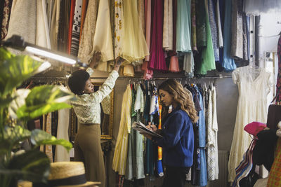 Female owner making notes while colleague arranging clothes in boutique