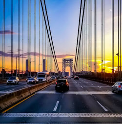 Cars moving on suspension bridge against sky during sunset
