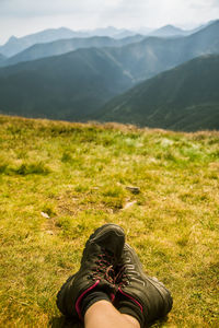 Low section of person on grass against mountains and sky