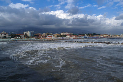 View of city at waterfront against cloudy sky