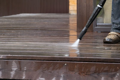 Man cleaning walls and floor with high pressure power washer. washing terrace wood planks 