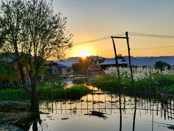 Scenic view of lake by buildings against sky during sunset