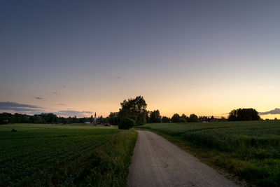 Road amidst field against sky during sunset