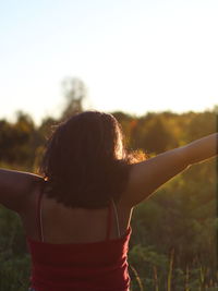 Rear view of woman with arms outstretched standing against sky