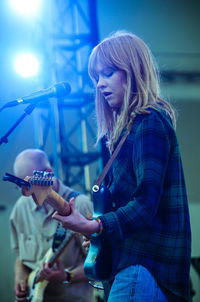 Young woman playing guitar while singing on microphone on stage