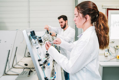 Side view of focused scientists in white uniforms setting up modern equipment for research while working together in light lab