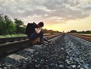 Man lying down on railroad track against sky