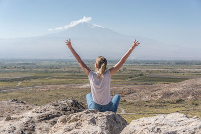 Rear view of woman sitting on rock against sky