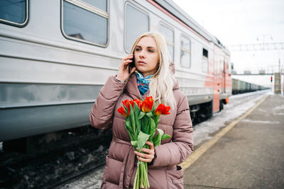 Girl on the station platform with tulip flowers talking anxiously on the phone