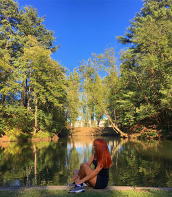 Woman sitting by lake against trees