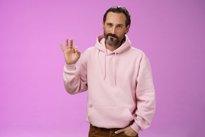 Portrait of man standing against pink background