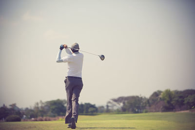 Rear view of golfer playing on field against clear sky