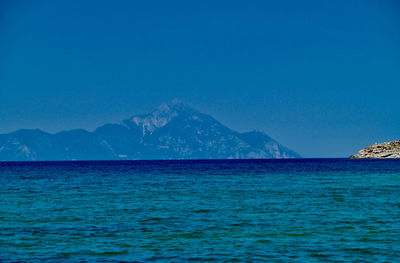 Scenic view of sea and mountains against clear blue sky