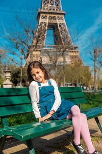 Young woman sitting on bench against trees