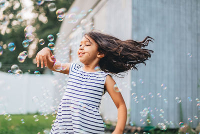 Diverse mixed race pre school girl outdoors during summer having fun in backyard with bubbles 