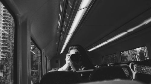 Woman photographing through camera while traveling in bus