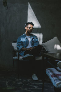 Young man looking away while sitting on sofa at home