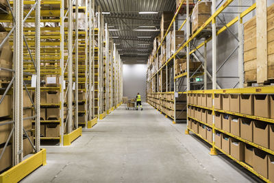 Mid distance view of senior male warehouse worker pushing cart on aisle in industrial building