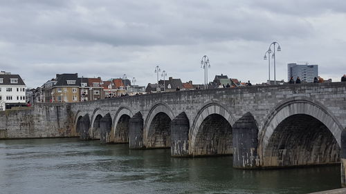 Arch bridge over river against sky in city