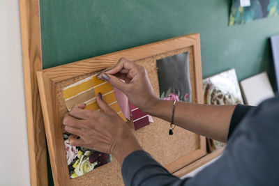 Cropped hands of businesswoman fixing color swatch with straight pins on bulletin board
