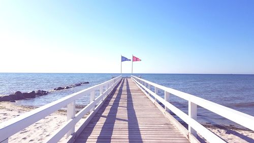 Pier over sea against clear blue sky