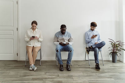 People using smart phones sitting on chairs in front of wall