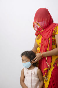 Mother wearing flu mask to girl against white background