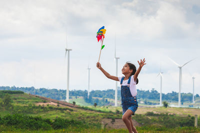 Girl playing with pinwheel toy on land with windmills in background