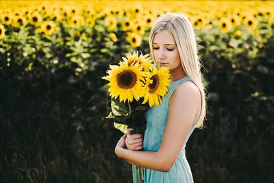 Young woman holding sunflowers on field