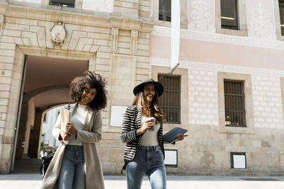 Smiling female coworkers walking on street against building in city