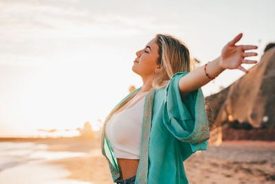 Side view of woman with arms raised standing at beach