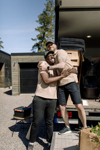 Happy delivery men embracing while standing outside truck