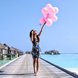 Woman with balloons walking on pier at beach against clear sky