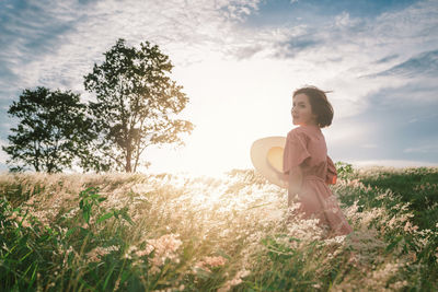 An asian girl on a beautiful spring meadow at sunset. she wears a pink dress and wide-brimmed hat.