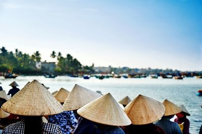 Woman wearing conical hats by lake against clear sky