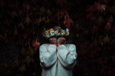 Woman wearing sweater covering face with flowers outdoors