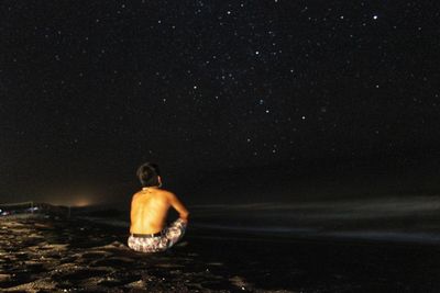 Rear view of shirtless man looking at sea against sky at night