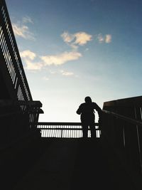 Silhouette man walking on bridge in city against sky